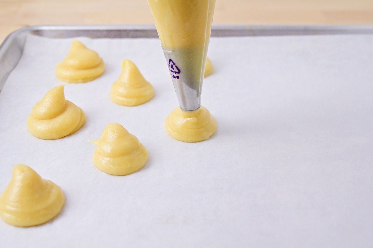 Piping cream puff dough onto a baking sheet.