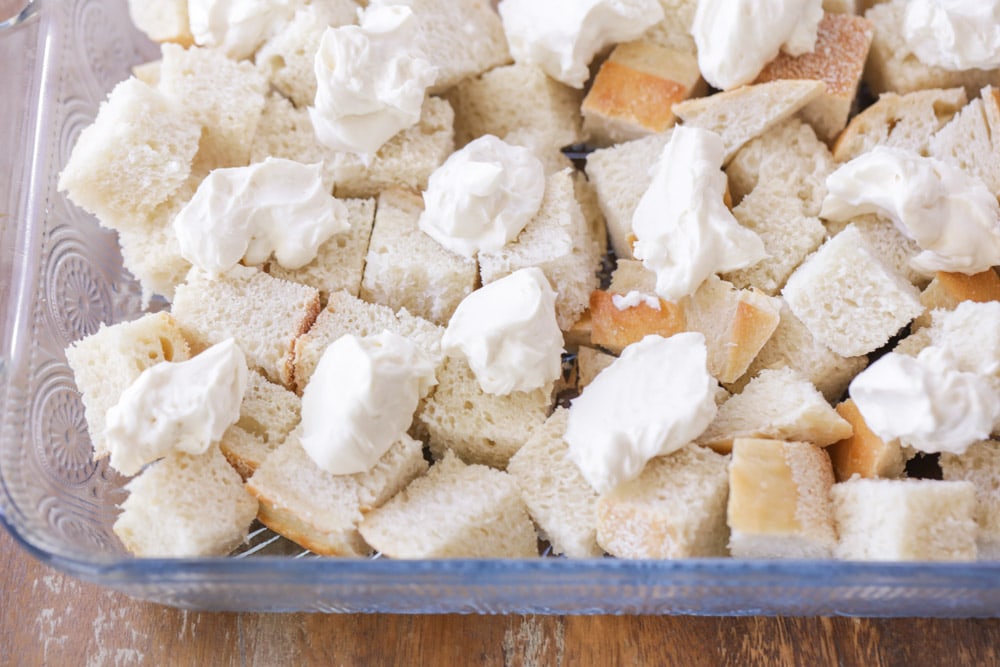 Bread cubes and dollops of cream cheese in a glass casserole dish.