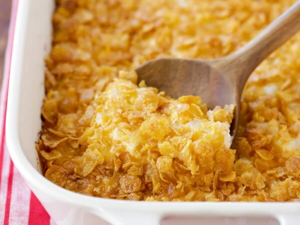 Funeral potatoes being scooped out of casserole dish.