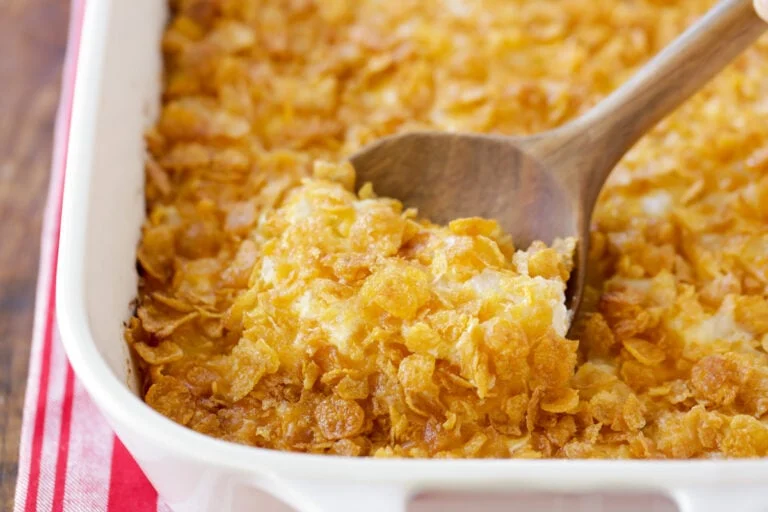 Funeral potatoes being scooped out of casserole dish.