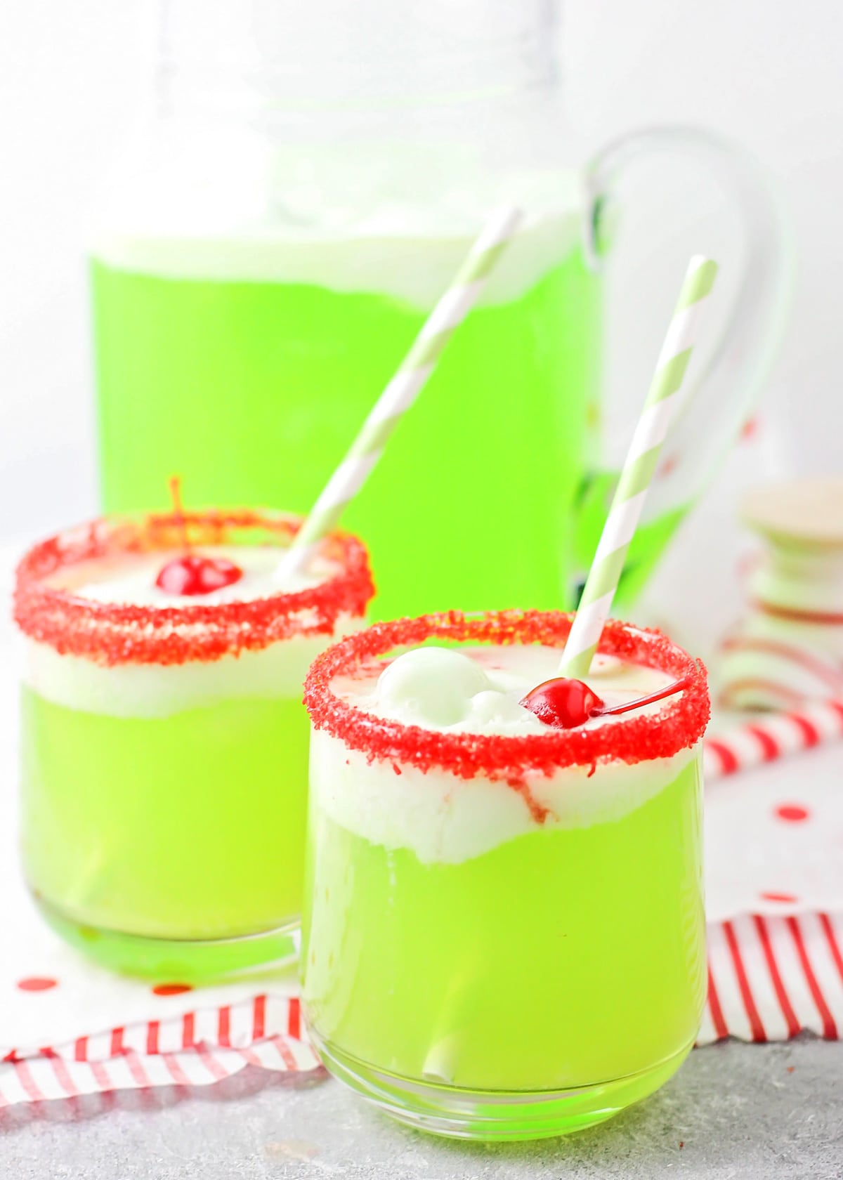 Two glasses of Grinch punch rimmed with red sugar and topped with cherries.