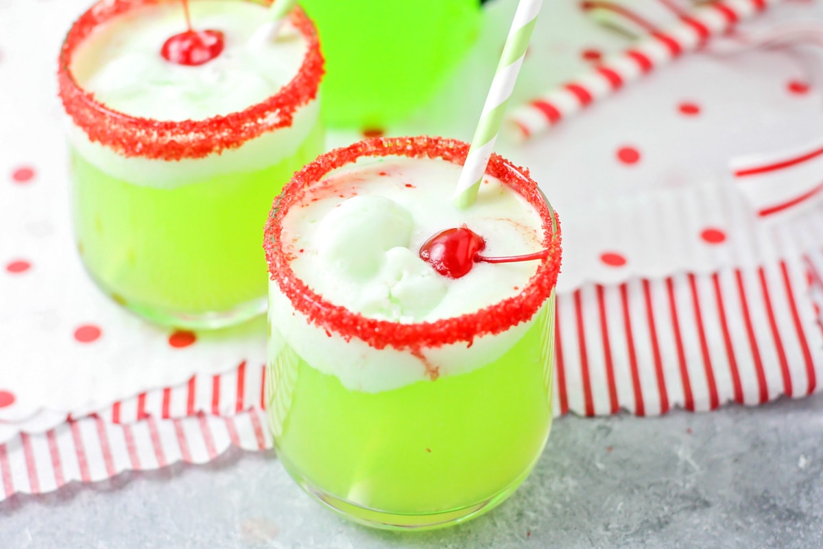 Two glasses of Grinch punch rimmed with red sugar and topped with a cherry.