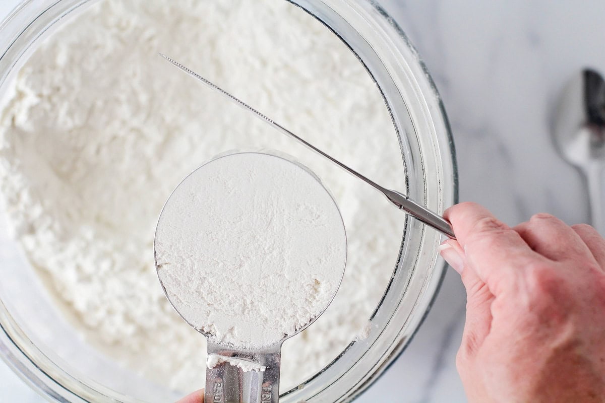 Flour being measured over a glass bowl.