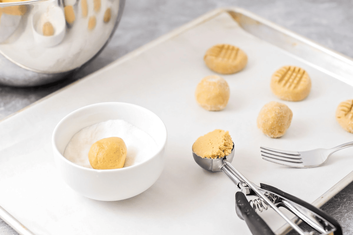 Scooping and coating peanut butter cookie dough balls in sugar.