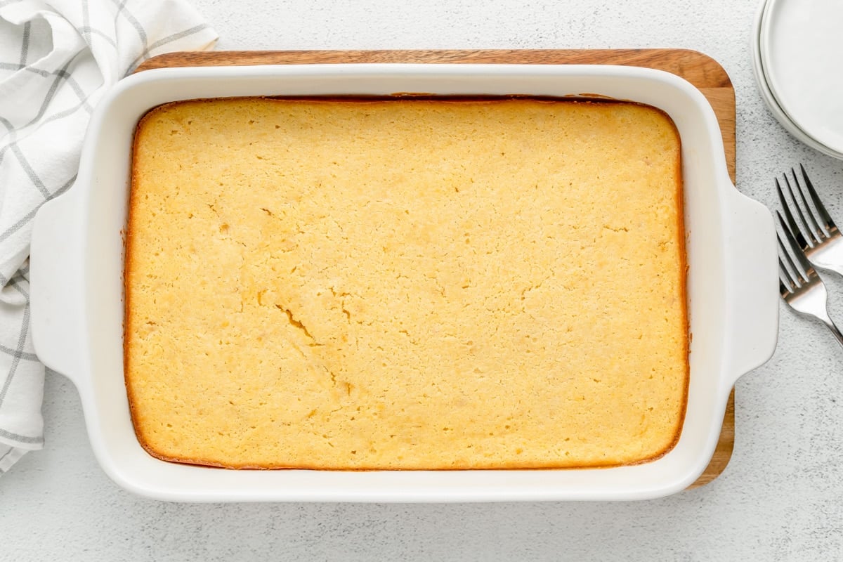 Baked jiffy corn casserole in a white casserole dish on the counter.