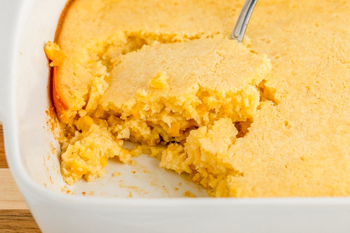 Scooping jiffy corn casserole from a white baking dish.