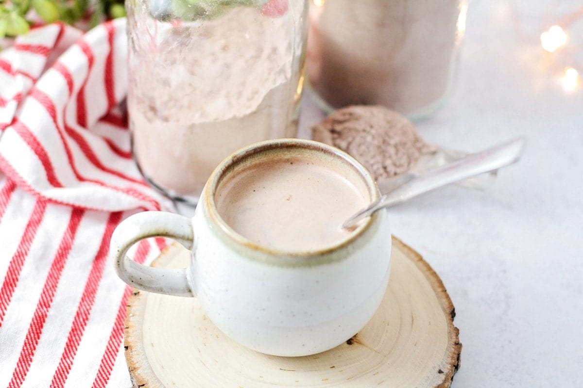 A cup of hot chocolate with a jar of cocoa powder behind it.