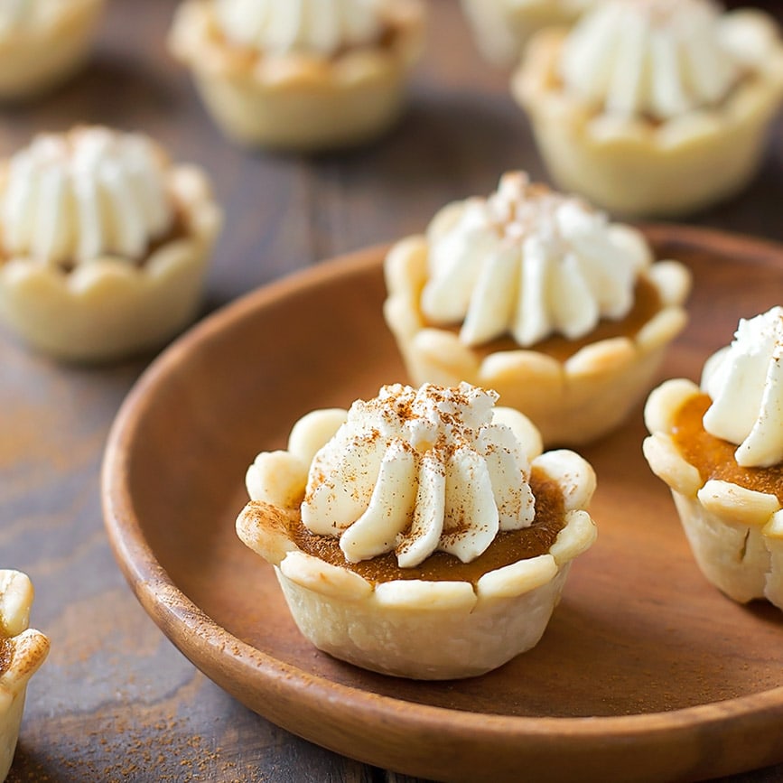 Mini Pumpkin Pies topped with whipped cream on a wooden bowl.