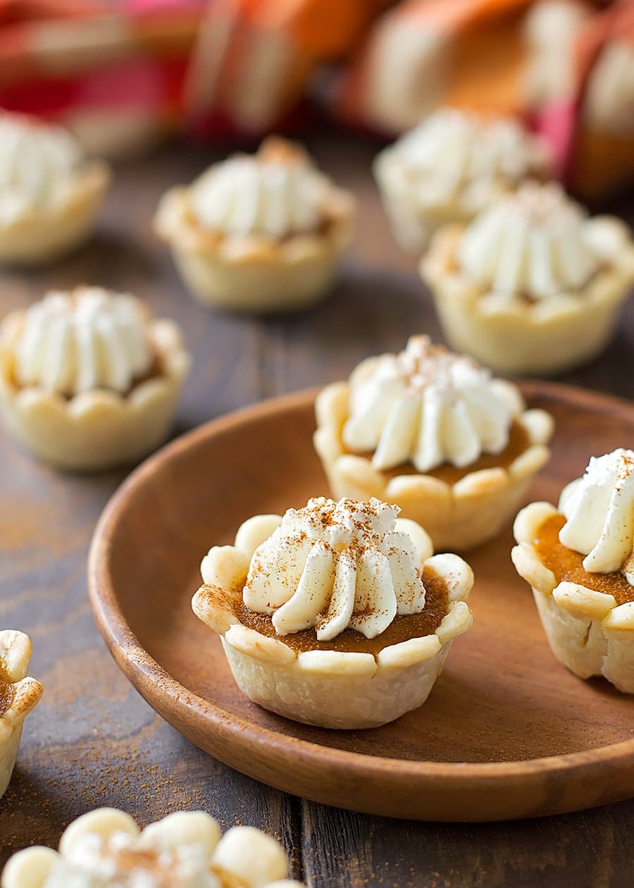 Mini Pumpkin Pie Bites topped with whipped cream and displayed on a wooden table.