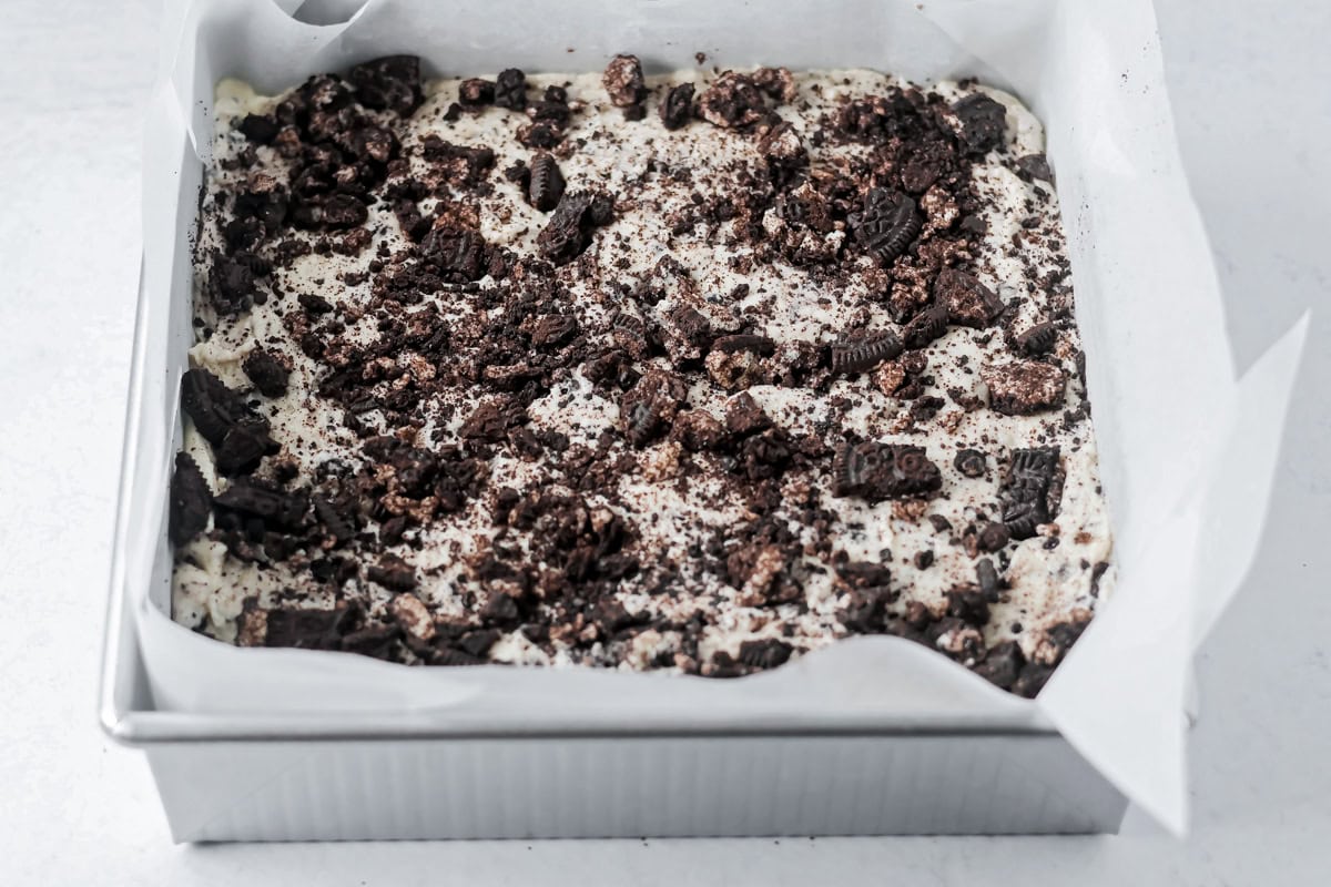 Adding crushed oreo to the top of oreo fudge.