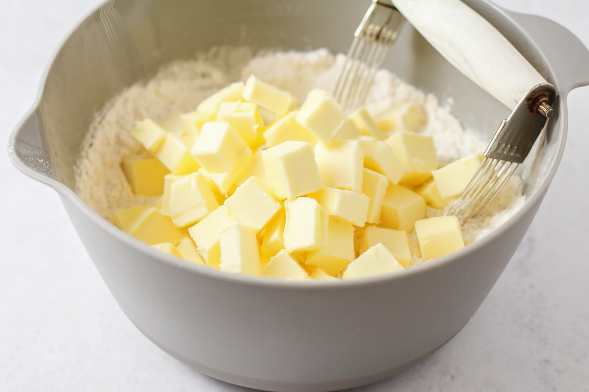 Adding cut butter to flour mixture in a grey bowl.