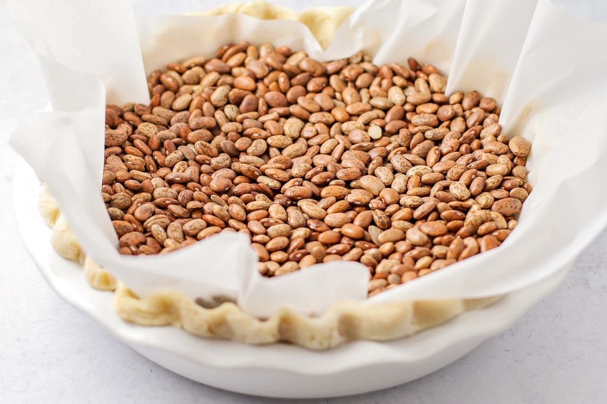 Homemade pie crust topped with parchment paper and filled with beans.