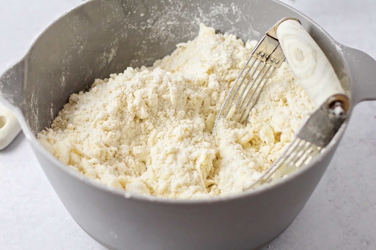 Cutting butter into flour mixture in a grey mixing bowl.