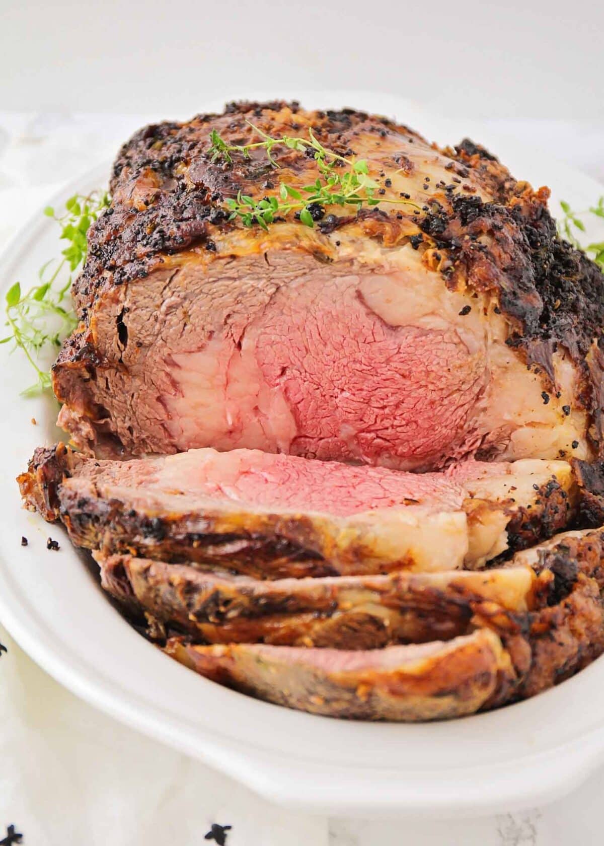 Prime rib recipe sliced in dish with fresh herbs on the side.
