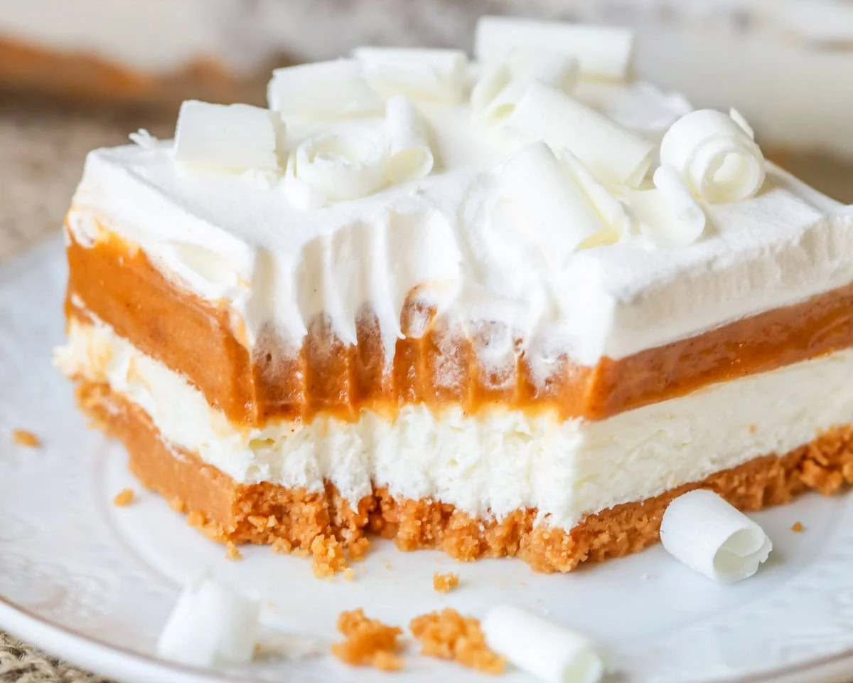 Pumpkin lasagna with layers of Oreos, cream cheese, pumpkin pudding, and whipped cream is a no-bake fall dessert that’s creamy and festive! Piece of pumpkin lasagna on white plate with bite taken out of it.