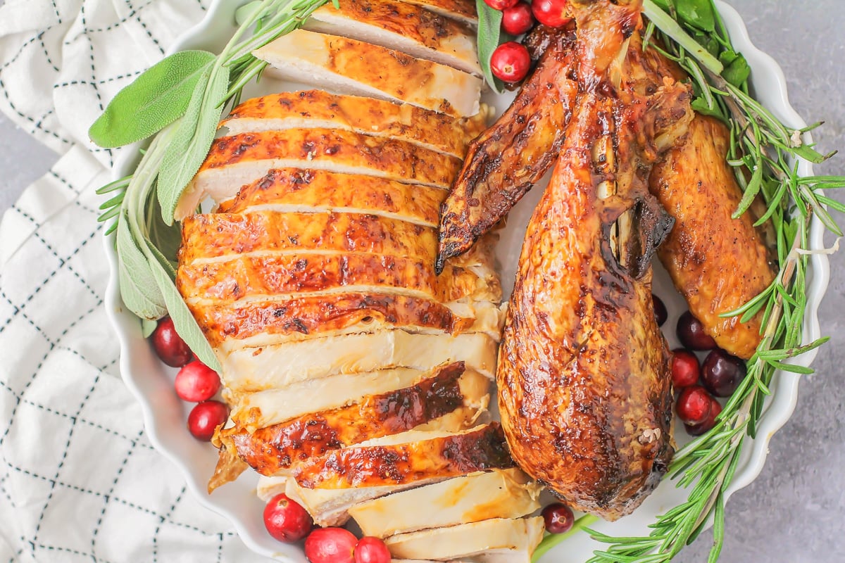 Close up of sliced roast turkey in dish with herbs and cranberries.