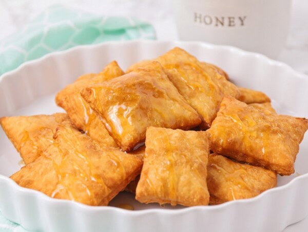 Several sopapillas on a platter drizzled with honey.