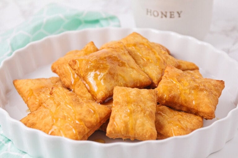 Several sopapillas on a platter drizzled with honey.