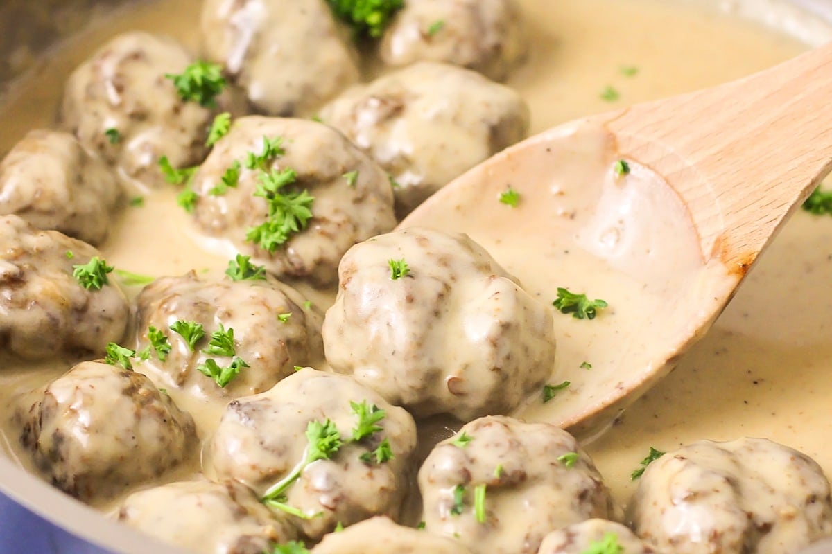 Easy Swedish meatballs recipe being scooped up with a wooden spoon.