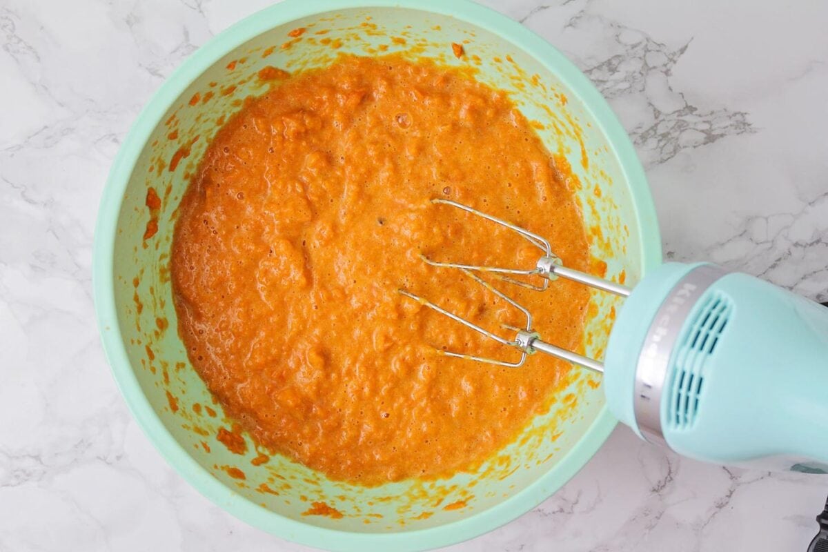 Creaming sweet potatoes with a hand mixer in a mint bowl.