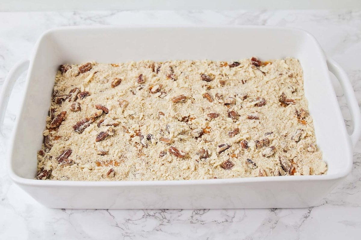 Adding pecan mixture to the top of the sweet potato spread.