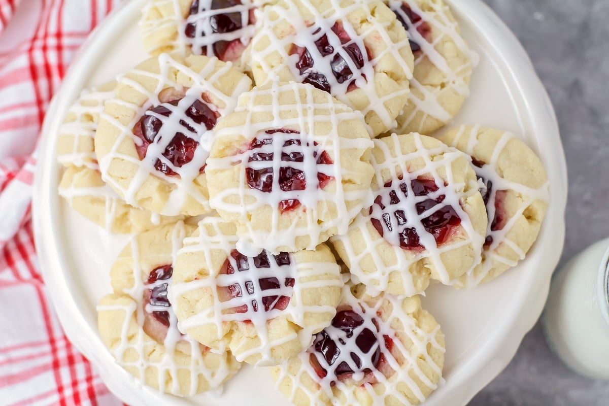 A plate filled with raspberry thumbprint cookies drizzled with glaze.