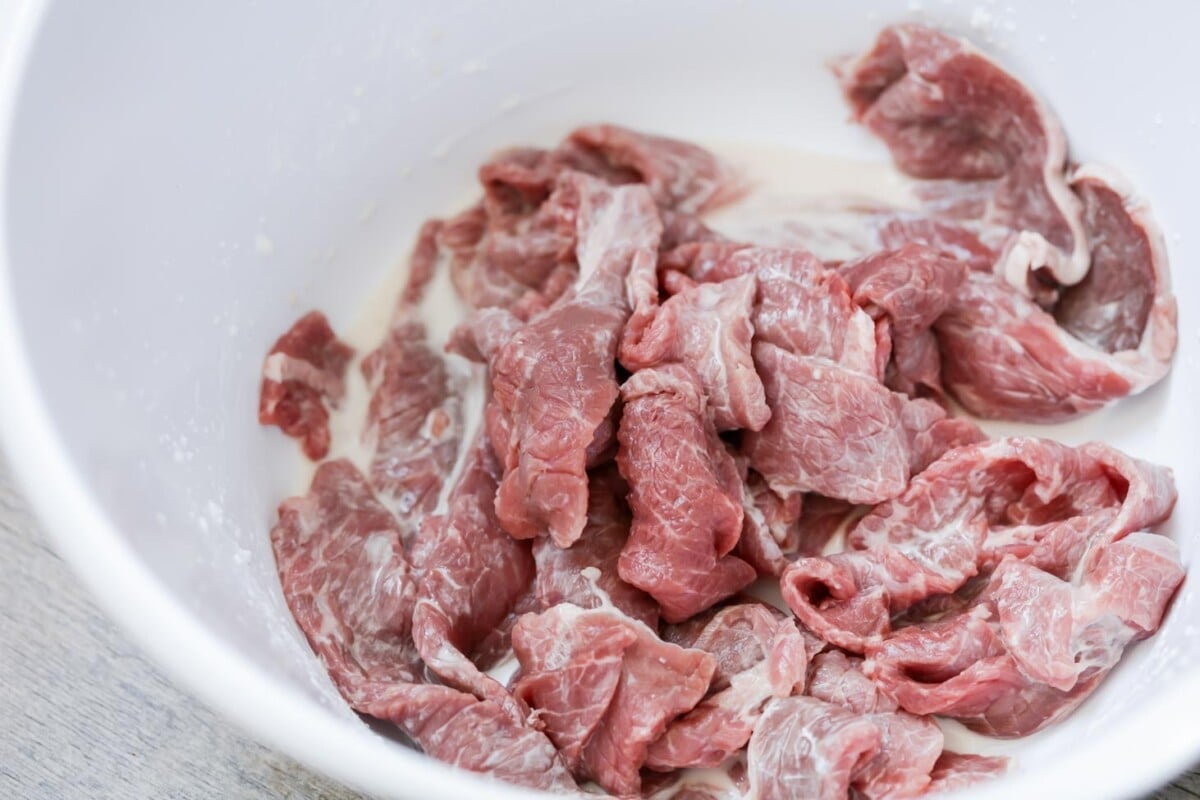 Beef strips marinating in a white bowl.