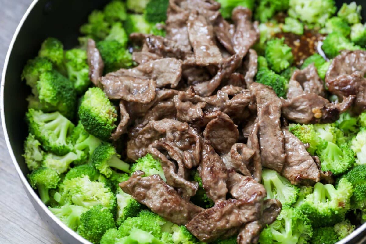 Beef strips added to cooked broccoli in a pan on the stove.