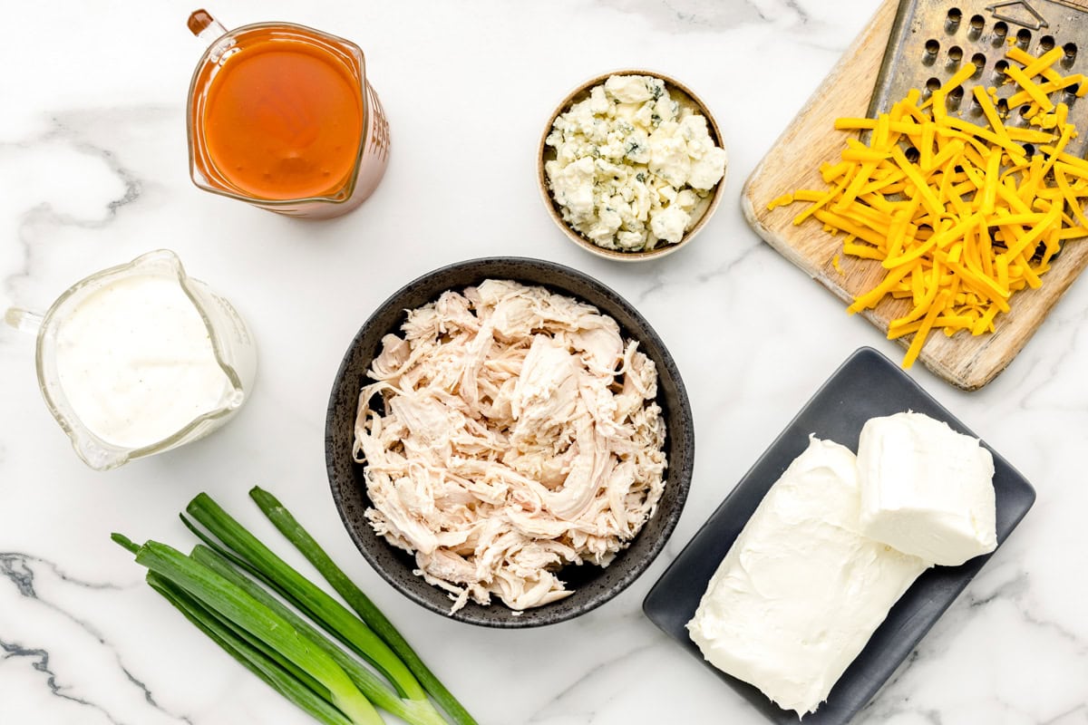 Ingredients for buffalo chicken dip on marble counter.