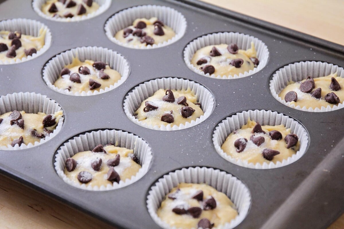 Homemade muffin batter topped with chocolate chips in a baking tin.