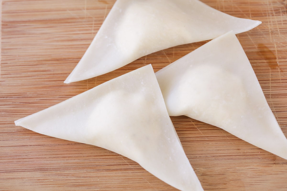 Folding wonton wrappers in half with filling inside.