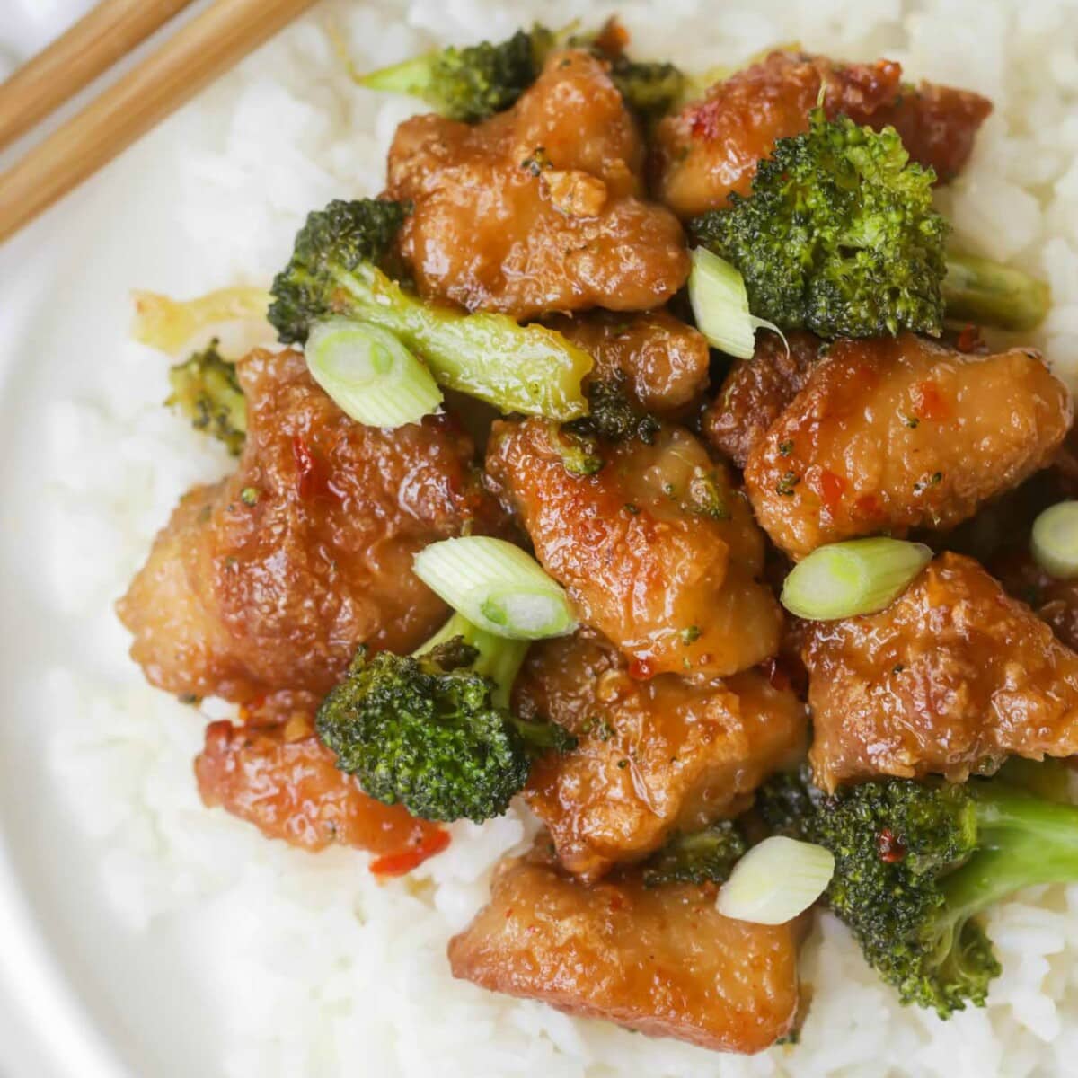 General Tso's chicken with broccoli served over white rice on white plate.