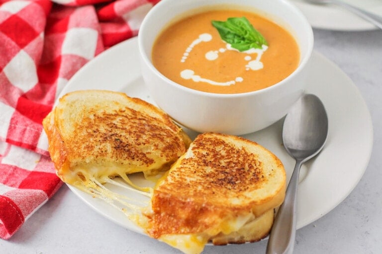 Grilled cheese recipe pulled apart on white plate served with tomato soup.