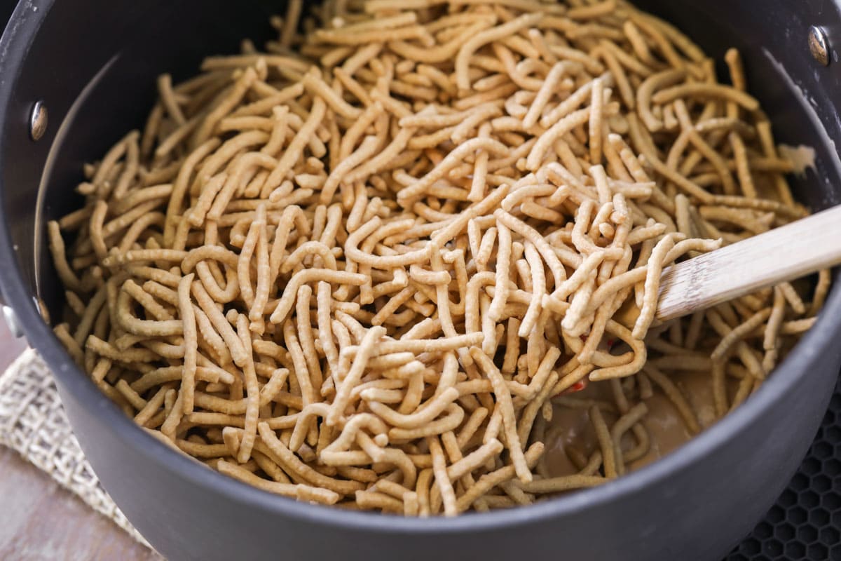 Adding chow mein noodles to a peanut butter mixture.