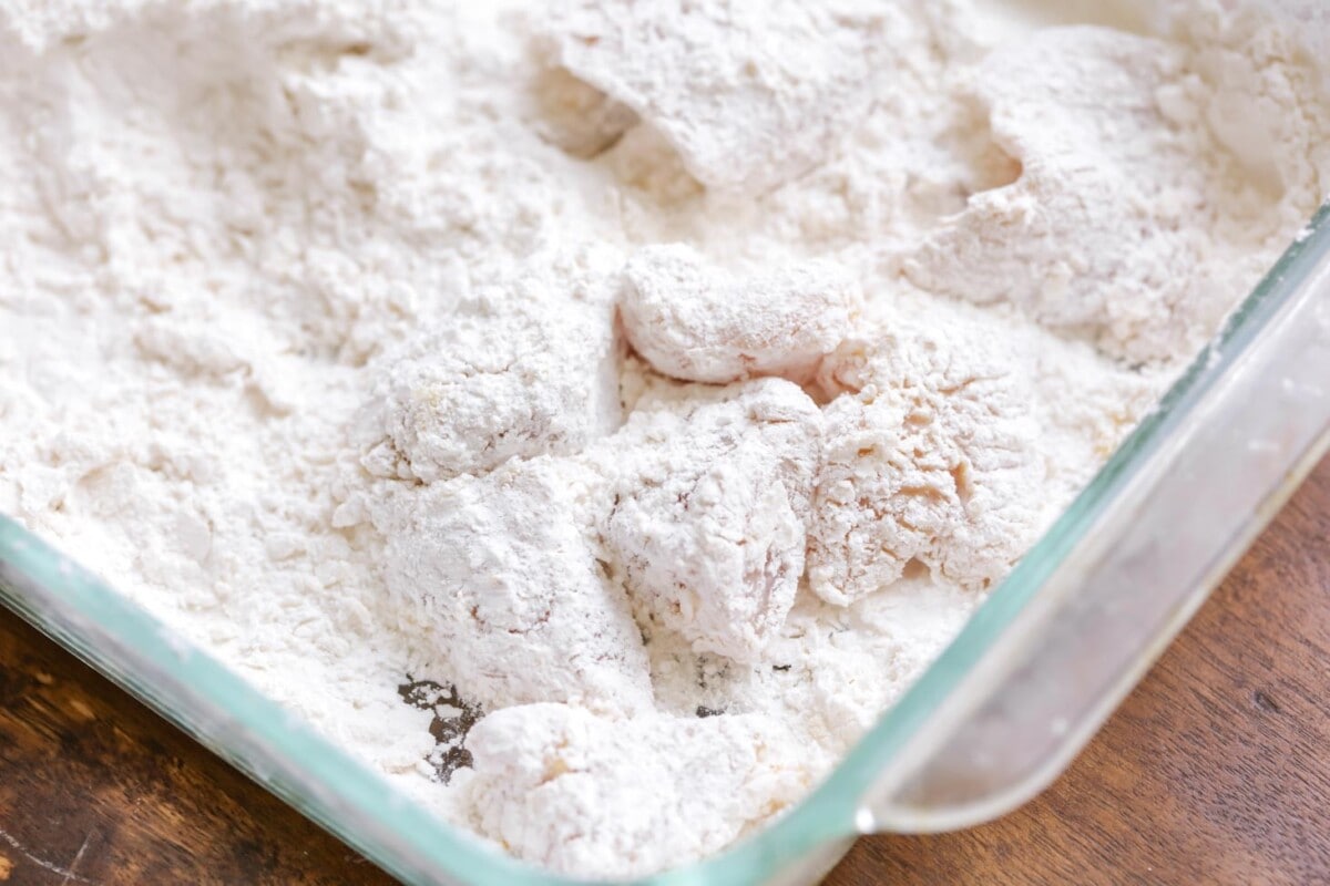 Flour coated chicken pieces in a glass baking dish.