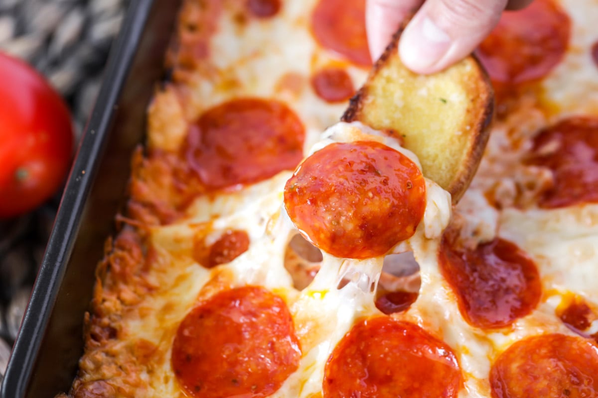 Close up of a bread slice being dipped into pizza dip.