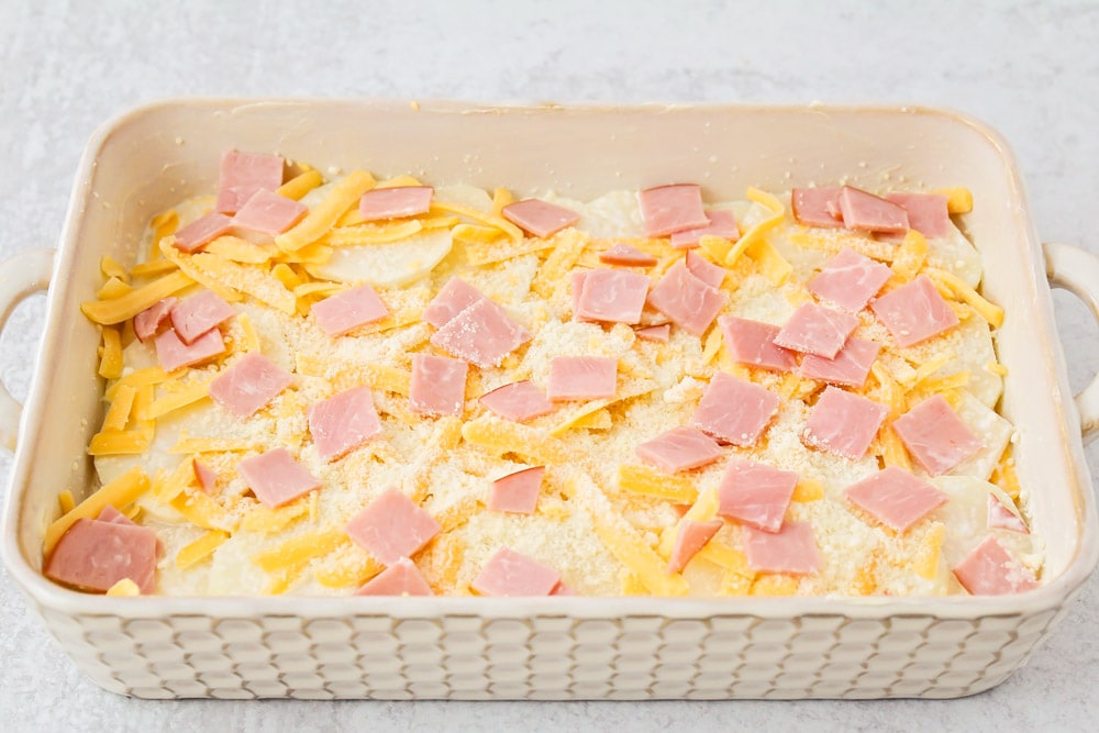 Layering potatoes, cheese, and ham in a casserole dish for scalloped potatoes and ham recipe.