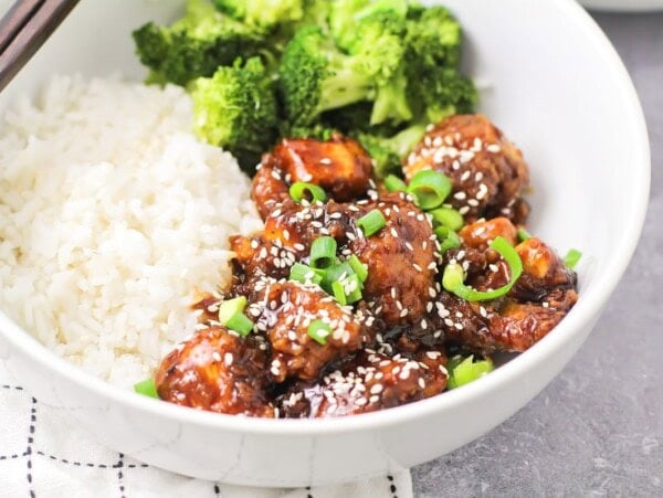 Sesame chicken served in a bowl with white rice.