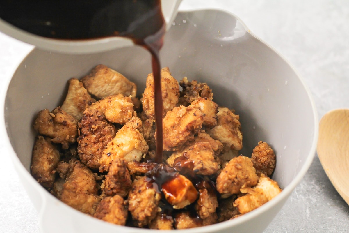 Sesame chicken sauce being poured over fried chicken pieces.