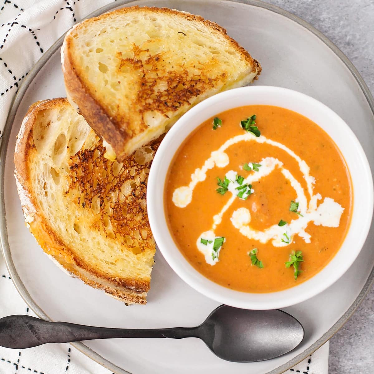 Tomato basil soup in bowl with grilled cheese on plate.