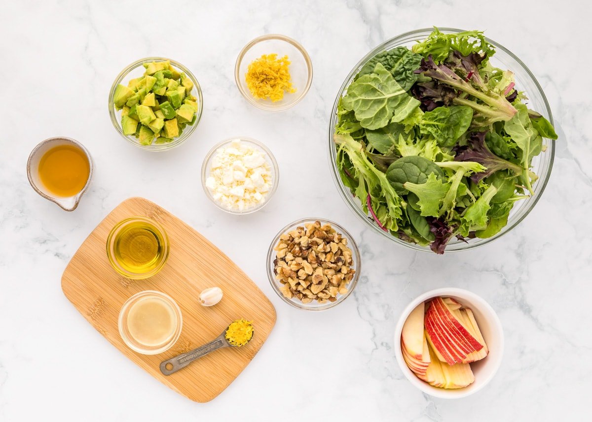 Lettuce, nuts, cheese, apples, and dressing ingredients measured on a kitchen counter.