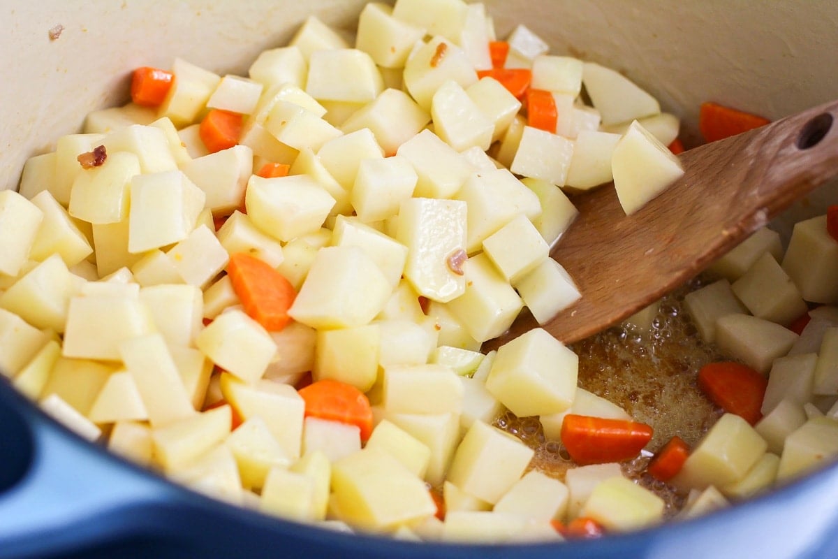 Cubed potatoes cooking with carrots in a pot.
