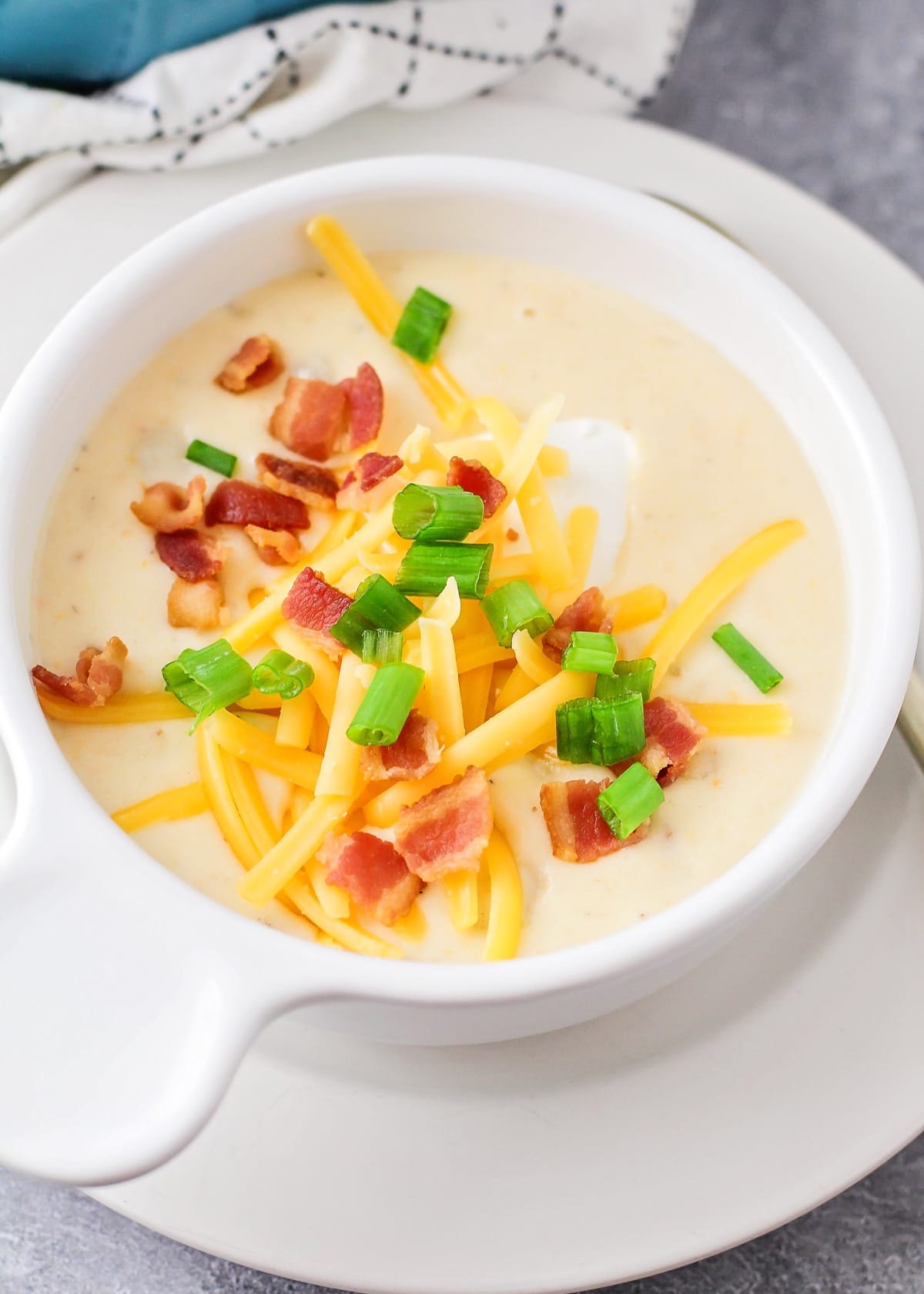Baked potato soup served in a white soup bowl with sour cream, green onion, bacon, and cheese served on top.