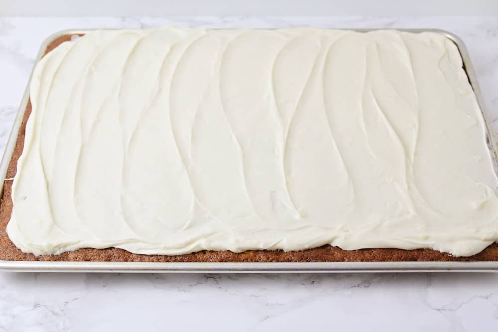 Cream cheese frosting spread onto carrot cake in a jelly roll pan.