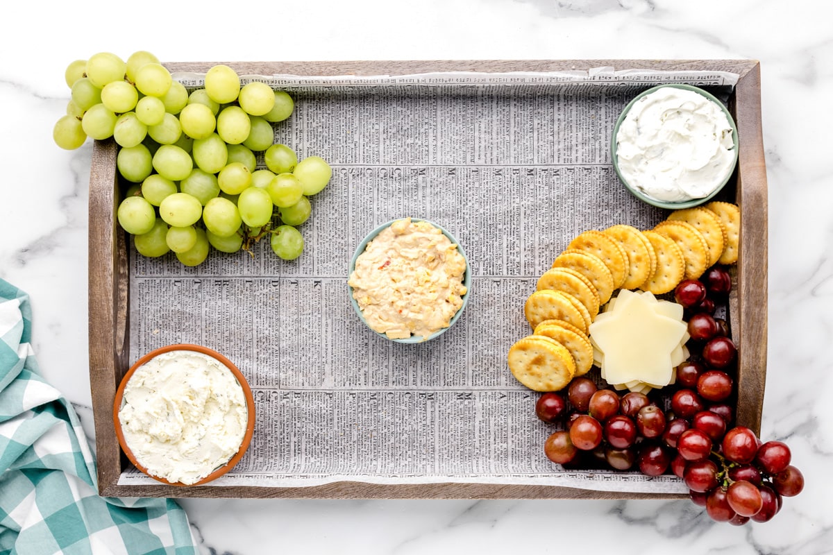 Adding grapes to the dips and crackers on a board.