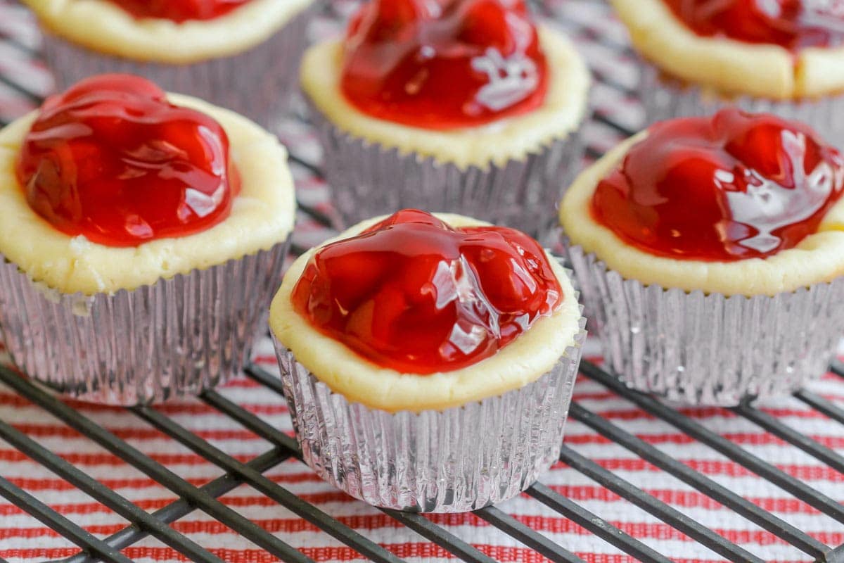 Mini cherry cheesecakes in cupcake liners on a wire rack.