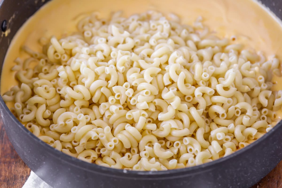 Elbow macaroni poured into sauce in skillet for slow cooker Mac and Cheese recipe.