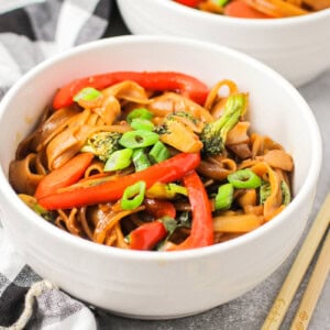 Drunken noodles recipe in white bowl with chopsticks on the side.