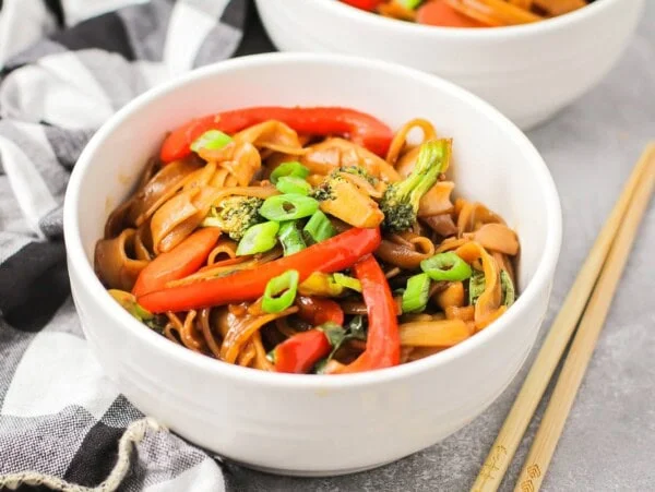 Drunken noodles recipe in white bowl with chopsticks on the side.