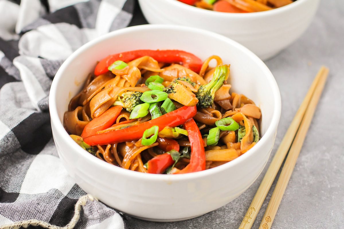 Drunken noodles in white bowl with chopsticks on the side.